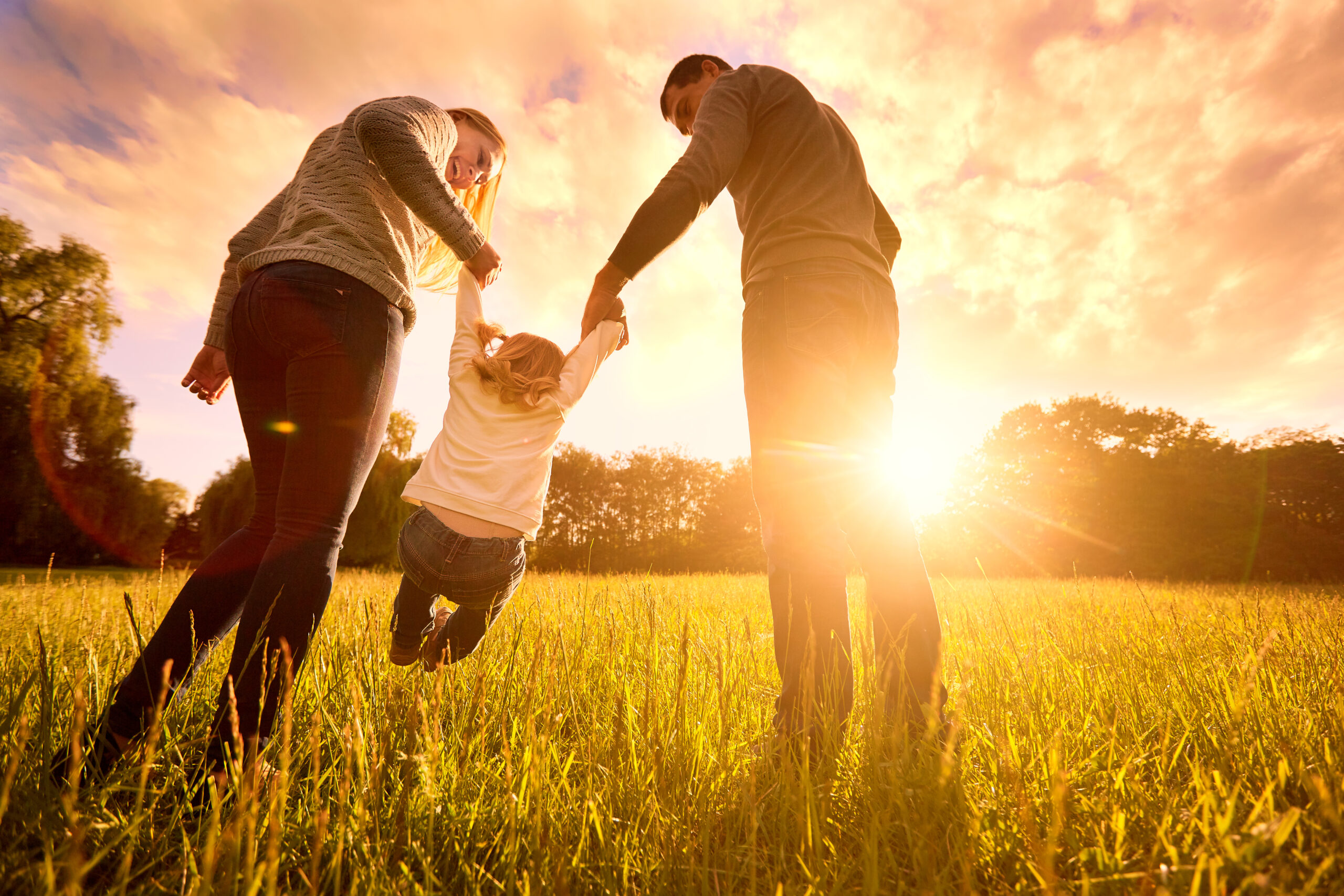 Parents hold baby's hands. Happy family in park evening